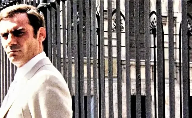 Gianmaria Volontè in una scena di Indagine su un cittadino al di sopra di ogni sospetto ripreso davanti ad un grande cancellata